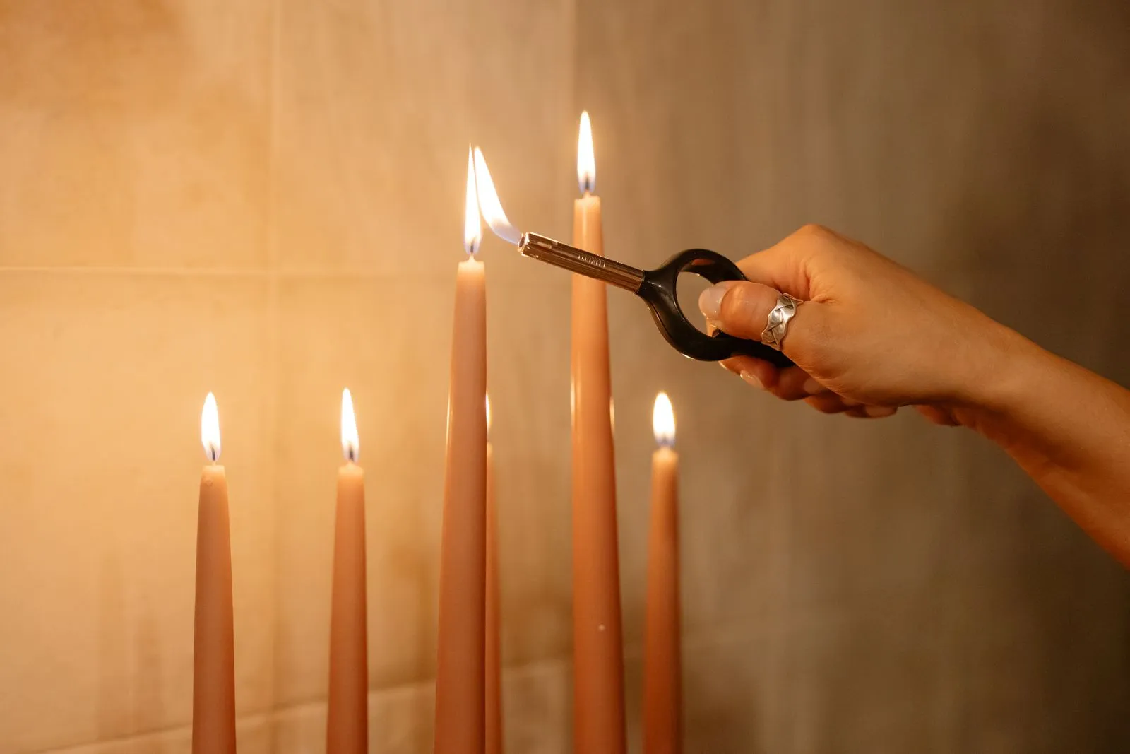 A hand lighting a row of tall tapers with a long lighter