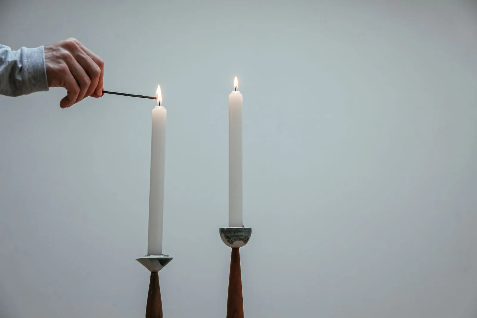 A hand lighting one of two tall white tapers in wooden holders